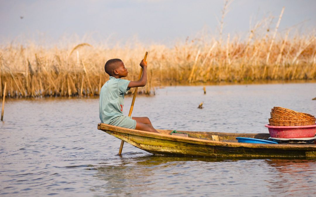 A boy rowing a small canoe on a boat in an unspecified country in Africa